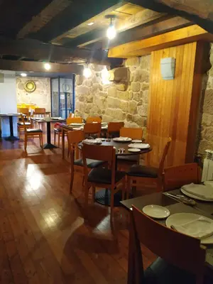 a restaurant with tables and chairs and a stone wall at Pensión rural Pallabarro in Allariz