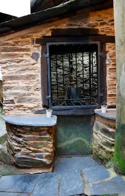 a window with bars on the side of a building at A casa do pozo - AS CASAS DO POZO - in Folgoso