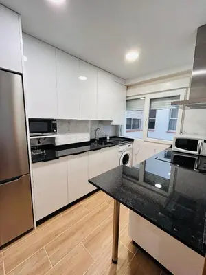 a kitchen with white cabinets and a black counter top at Apartamento San José in Milladoiro