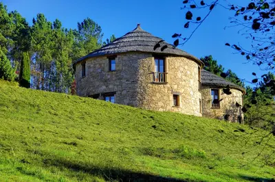 an old stone house on a grassy hill at Hotel Balneario Río Pambre in Palas de Rei