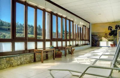 a waiting room with windows and tables and chairs at Hotel Balneario Río Pambre in Palas de Rei