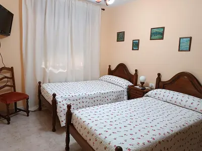 a bedroom with two beds and a chair and a window at PENSIÓN* AS VIÑAS in Puebla del Brollón