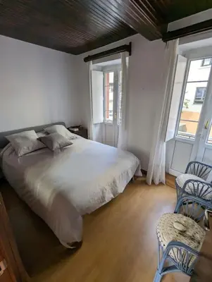 a bedroom with a bed with two chairs and two windows at Casa Buenos Aires in Ribadeo