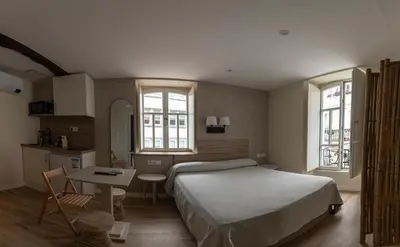 a bedroom with a bed and a table and two windows at NOARU Apartamentos Deluxe in Ares