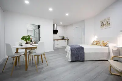 a white bedroom with a bed and a table and chairs at Huna Apartamentos in Padrón