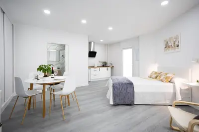 a white bedroom with a bed and a table and chairs at Huna Apartamentos in Padrón
