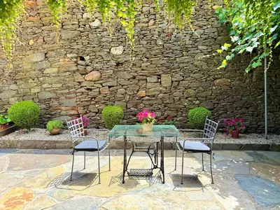 a table with three chairs and a stone wall at O Val de Vilaboa in Bóveda