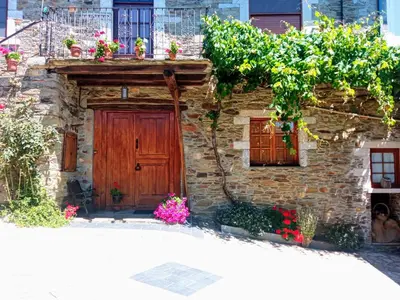 a stone house with a wooden door and flowers at O Val de Vilaboa in Bóveda