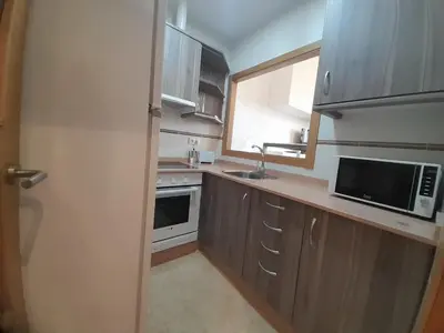 a kitchen with wooden cabinets and a microwave and a window at EnViveiro a pie de Playa de Covas II in Viveiro