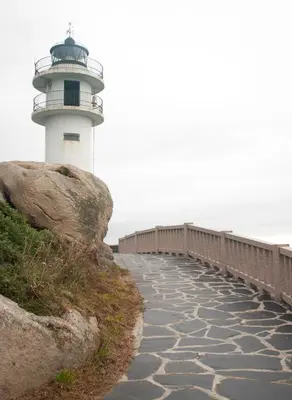 a lighthouse on a cliff next to a bridge at EnVIVEIRO Destino Playa de Covas in Viveiro