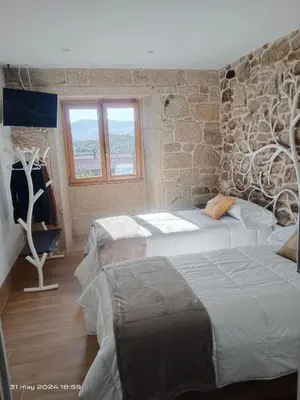 a bedroom with two beds and a stone wall at Casa Desigual in Padrón