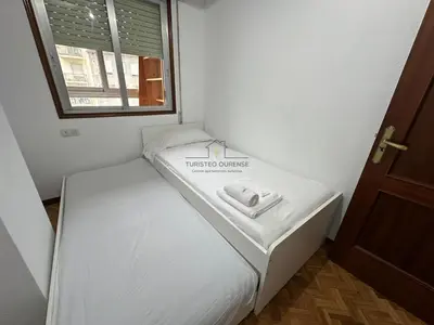a small white bed in a room with a window at O Rincón de Laly in Ourense