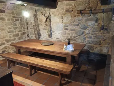 a wooden table and benches in a room with a stone wall at Lareira rural apartamento Ribeira Sacra Chantada in Chantada
