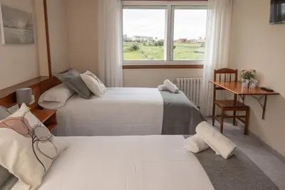 two beds in a room with a window and a table at Pensión A Codeseira Melide in Melide