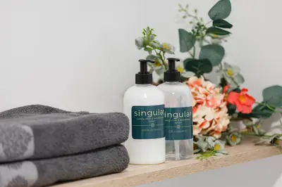 two bottles of shampoo and towels on a shelf with flowers at Luxury Singular Apartments Orange in Santiago de Compostela