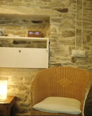 a wicker chair sitting next to a stone wall at Pensión con Encanto San Martiño Pinario in Santiago de Compostela