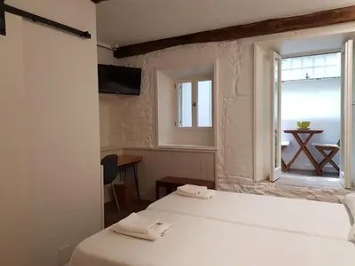 a room with two beds and a window with a table at Pensión con Encanto San Martiño Pinario in Santiago de Compostela