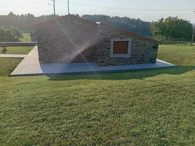 a stone house with a sprinkler in a field at Eira do Xastre in Brocos