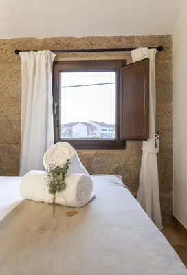 a bedroom with a bed with a chair with a window at O Fogar da Pequena Galia in Caldas de Reis