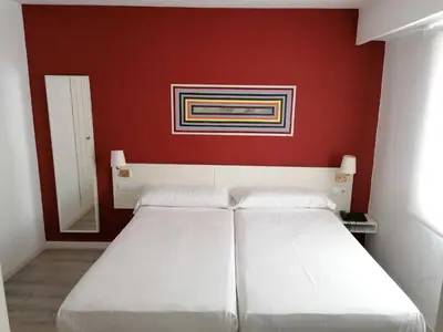 two beds in a room with a red wall at Hotel Miño in Ourense