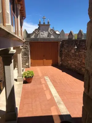 a brick courtyard with a building with a gate and a cross at Casa do Ferreiriño in Chacente