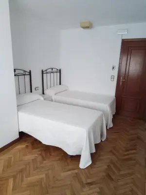 two beds in a room with white walls and wooden floors at Pensión La Plaza in Betanzos