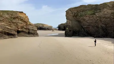 a person standing on a beach between two large rocks at Apartamento Playa las catedrales in Foro