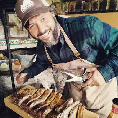 a man in an apron cutting a pile of meat at Somiedoeco in Caunedo