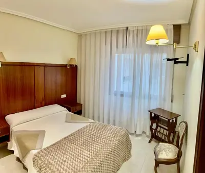 a bedroom with a bed and a table and a window at Hostal La Cubana in Carballino