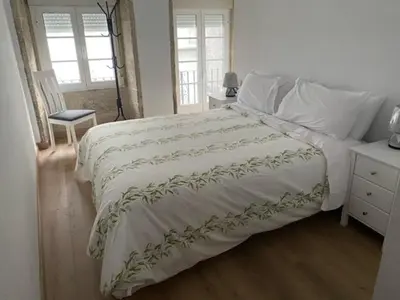 a bedroom with a bed and a chair and windows at o piso de loli e manolo in Santiago de Compostela