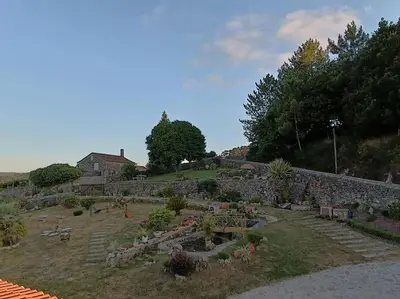 a garden with a stone wall and trees and a building at Casa Labrega da Torre in Silleda