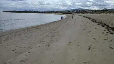 two people walking along a sandy beach near the water at Refugio de mar in Barreiros