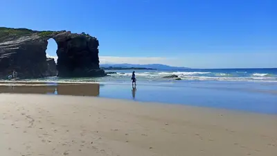 a person standing on a beach with an arch in the ocean at AYE Catedrales in Barreiros