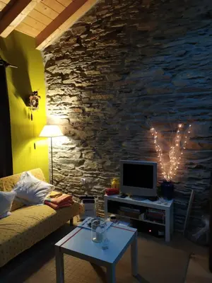 a living room with a tv and a stone wall at Refugio Alto Sil in Páramo del Sil
