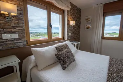 a bedroom with a bed with two pillows and two windows at Hotel el Pinar in Villapedre