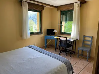 a bedroom with a bed and a desk and two windows at Rural Coliving in Pontevedra