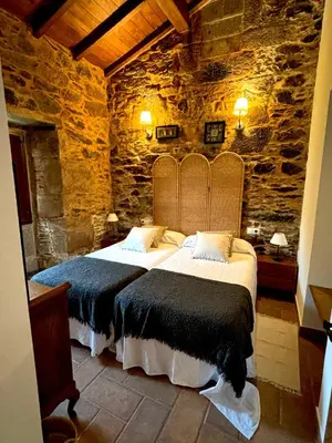a bedroom with two beds and a stone wall at As Casiñas Bed & Breakfast Porto de Bois in Palas de Rei