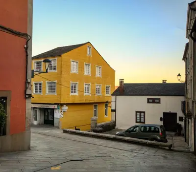 a yellow building with a car parked in a street at Pension Escalinata in Sarria