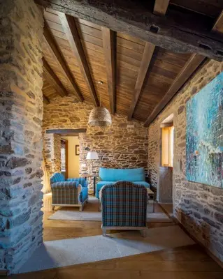 a living room with blue chairs and a stone wall at Casa Peón de Pardaces in Santiago de Compostela