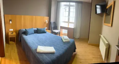 a bedroom with a blue bed and a television at Pension Luscofusco in Puebla de Trives