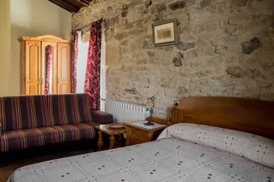a bedroom with a bed and a couch in a stone wall at Casa Roan y Casa Grande in Lodoso