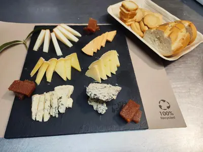 a black cutting board with cheese and bread on a table at Hotel Restaurante Las Camelias in Jarrio