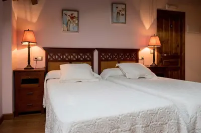 a bedroom with two beds with white sheets and two lamps at Hotel Rural Casona Trabadelo in Vegadeo