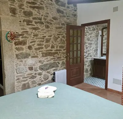 a bedroom with a stone wall and a table with towels at Casita Meu Pai in Boimorto