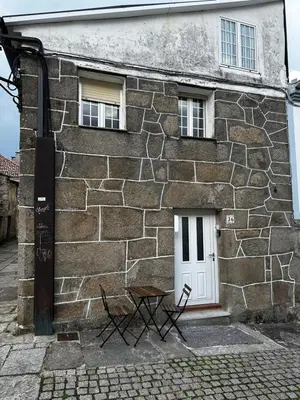 a stone building with a white door and a chair outside at A Ribeira in Castro Caldelas