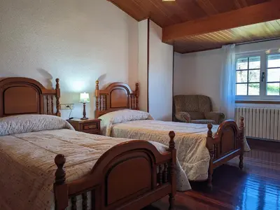 a bedroom with two beds and a chair and a window at Casa Filomena in Santiago de Compostela