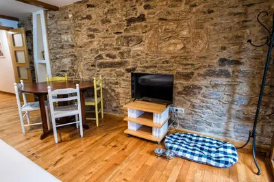 a room with a stone wall with a table and a television at Alda Fogar Natural in Santiago de Compostela