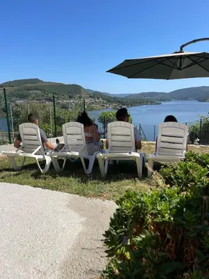 three people sitting in lawn chairs under an umbrella at Casa da Ramona in Ribadavia