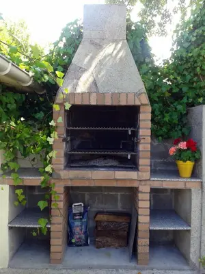 a outdoor brick oven with flowers in a garden at Gran chalet con jardín, piscina y BBQ in Sada