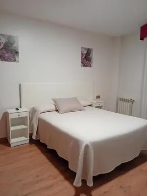 a white bedroom with a white bed and a night stand at El Ancla in Ponferrada